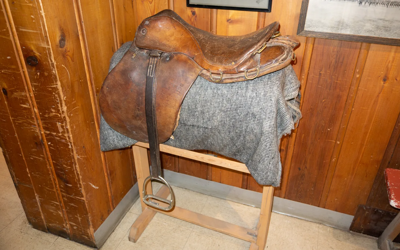Gebrauchter brauner Ledersattel mit Filzunterlage auf einem hölzernen Sattelbock